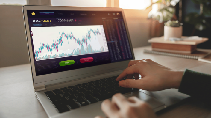 A person trading cryptocurrencies on a laptop, with a focus on a cryptocurrency investments chart showing price movements.